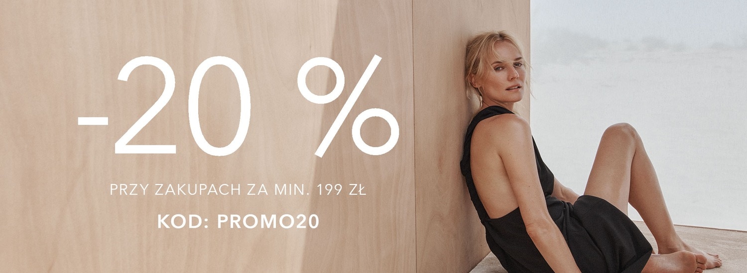 Skorzystaj z promocji -20% na zakupy za min. 199 zł z kodem: PROMO20, modelka w czarnej sukience pozuje na tle beżowej ściany.