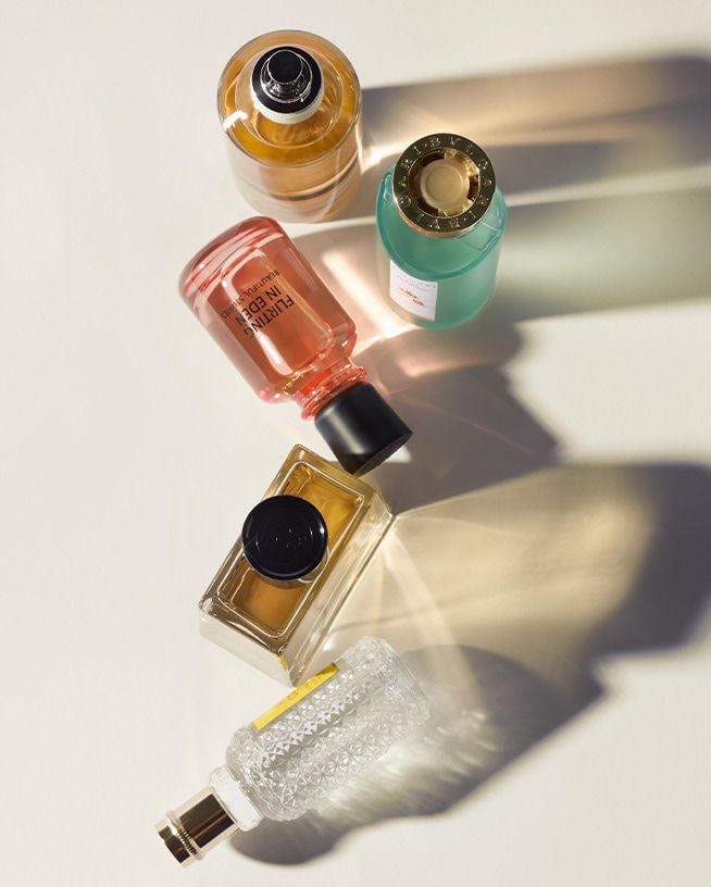 Na białym tle leżą flakony perfum w odcieniach bursztynu, różu i błękitu, tworząc elegancką kompozycję.